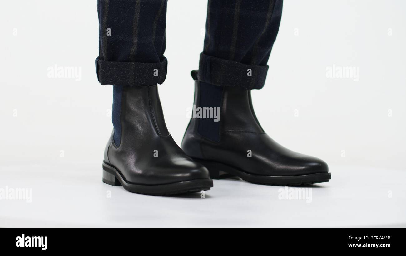 Schwarze Chelsea-Boots aus Leder, kombiniert mit karierten Hosen, präsentieren modernen Herrenmode-Stil und elegante Schuhmode Stockfoto