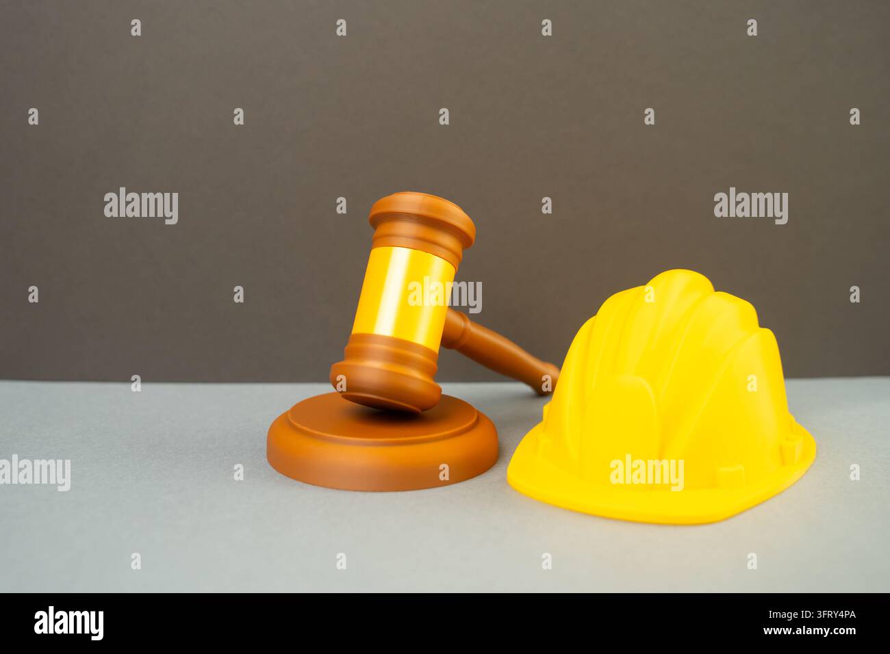 Ein gelber Sicherheitshut und ein Richterhammer. Konzept der gesetzlichen Compliance in der Bauindustrie und Sicherheitsstandards. Regulierung von Bau und Renovierung Stockfoto
