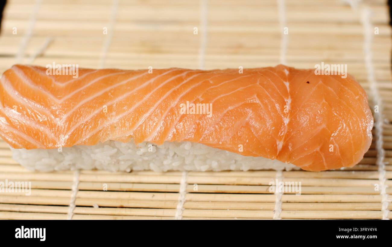 Lachs-Sushi-Nigiri, die auf einer Bambusmatte zubereitet wird, zeigt frischen rohen Fisch und weißen Reis für die japanische Küche Stockfoto