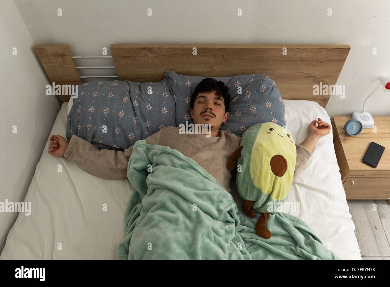 Oberansicht eines Mannes, der in seinem Bett liegt und tief schläft, während er seinen Schlafanzug trägt. Eine ruhige Szene, ideal für Konzepte von Ruhe und erholsamen Schlaf Stockfoto