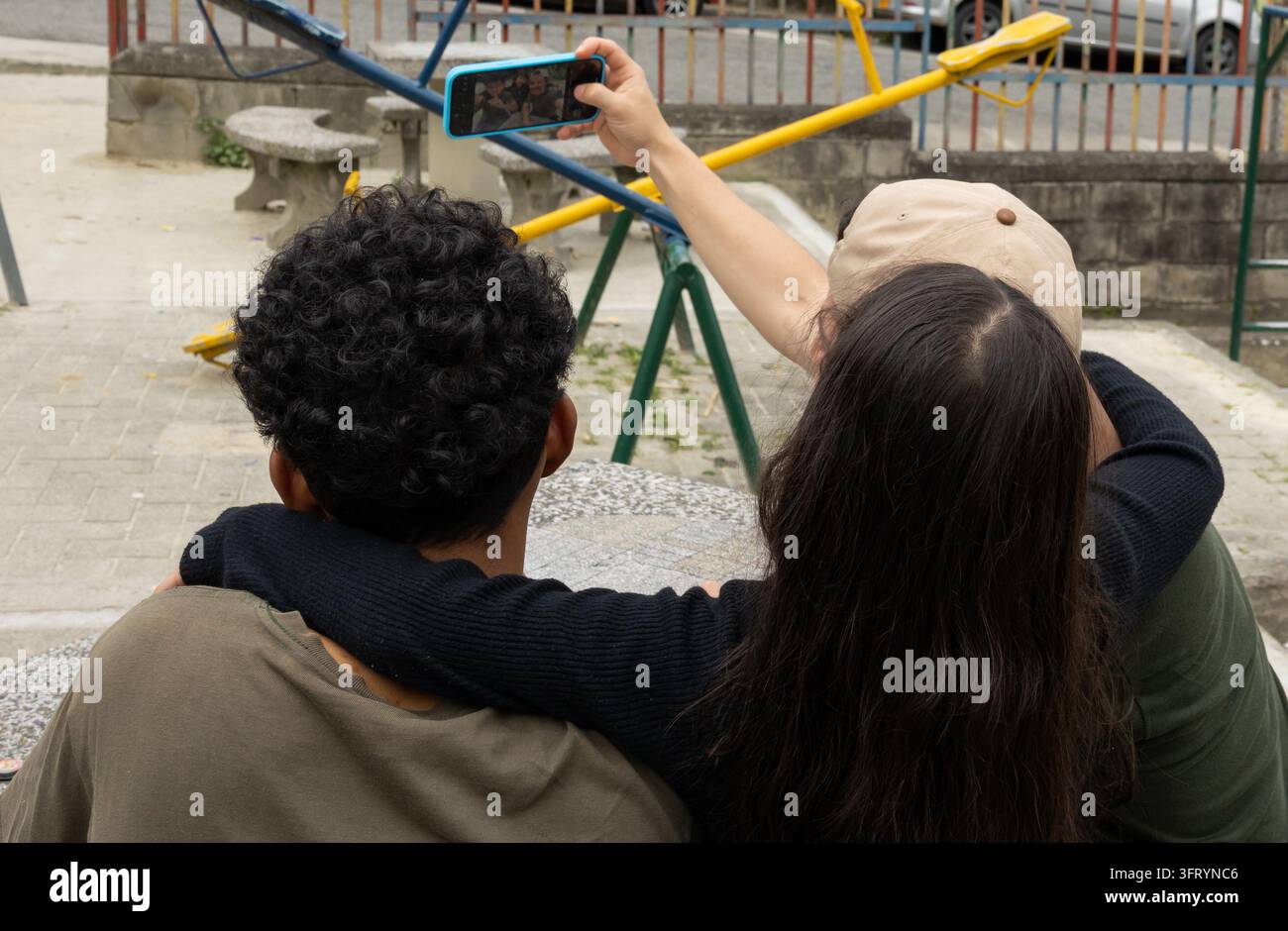 Mann mit seiner Nichte und seinem Freund, der von hinten in einem Park ein Selfie macht und einen alltäglichen sozialen Moment im Freien mit Mobiltechnologie einfängt Stockfoto