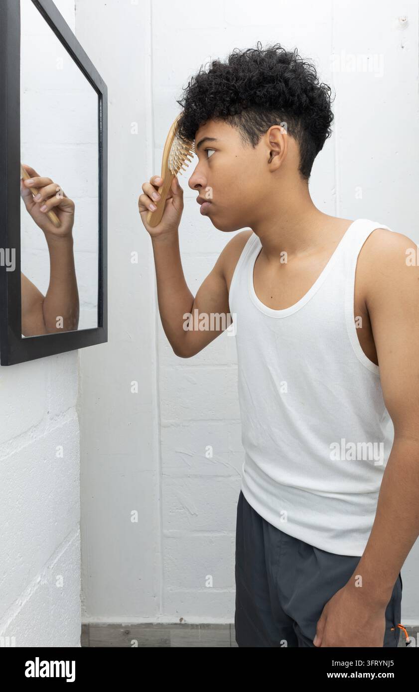 Dunkelhäutiger Teenager stylt seine Haare vor dem Spiegel, während er sich ruhig zu Hause fertig macht. Entspannte persönliche Routine, Selbstpflege, Alltagsleben Stockfoto