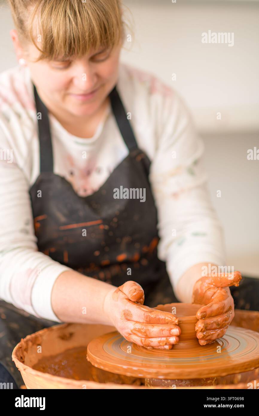 Töpferin stellt Steingut auf einer drehenden Töpferscheibe her, Hände formen nassen Ton zu einem neuen Stück während einer Workshop-Sitzung, konzentriert auf das Handwerk Stockfoto