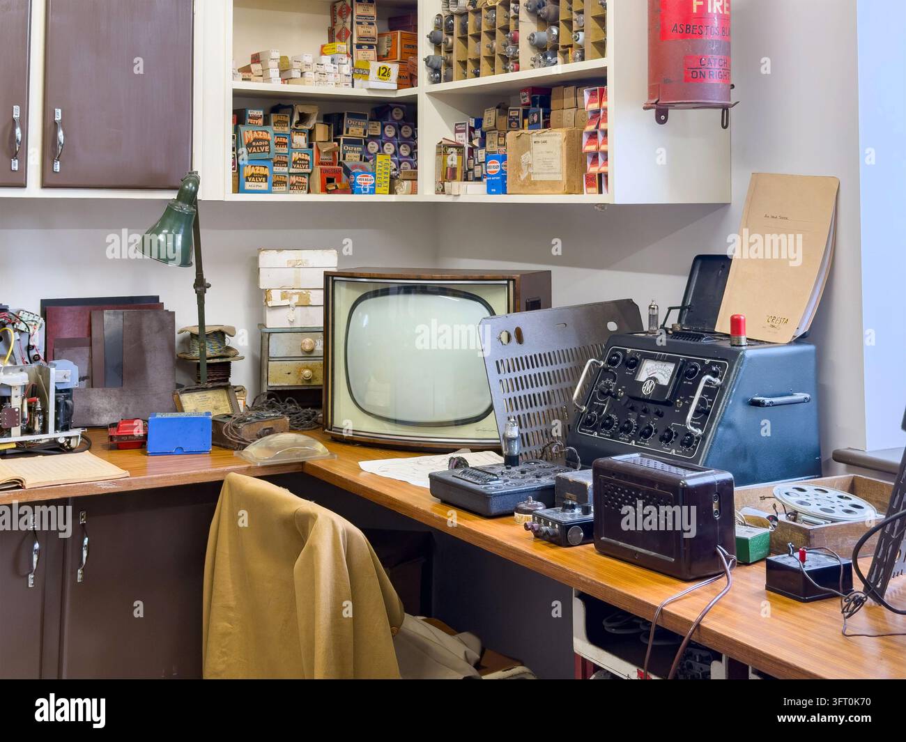 Vintage-Fernsehreparaturwerkstatt-Ausstellung mit braunem Monitor, Testgeräten, Ventilen, Radio, Werkzeugen, Regalen, Schreibtisch und Stuhl im Innenraum Stockfoto