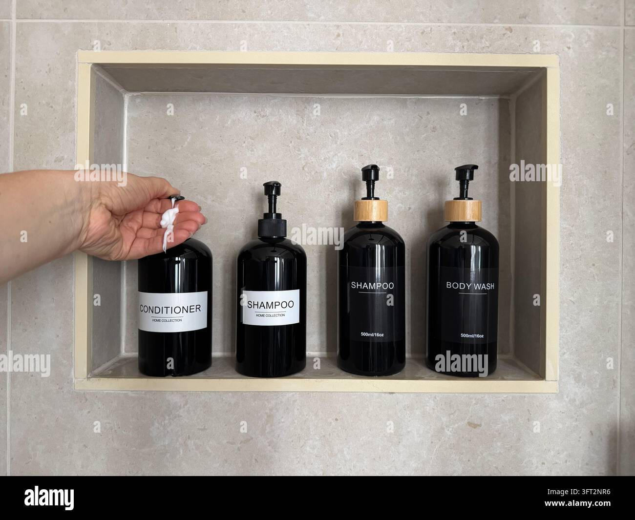 Hand verteilt Spülung aus einer nachfüllbaren Pumpflasche in einer eingebauten Duschnische mit Shampoo- und Körperwaschbehältern. Badezimmerorganisation. Stockfoto