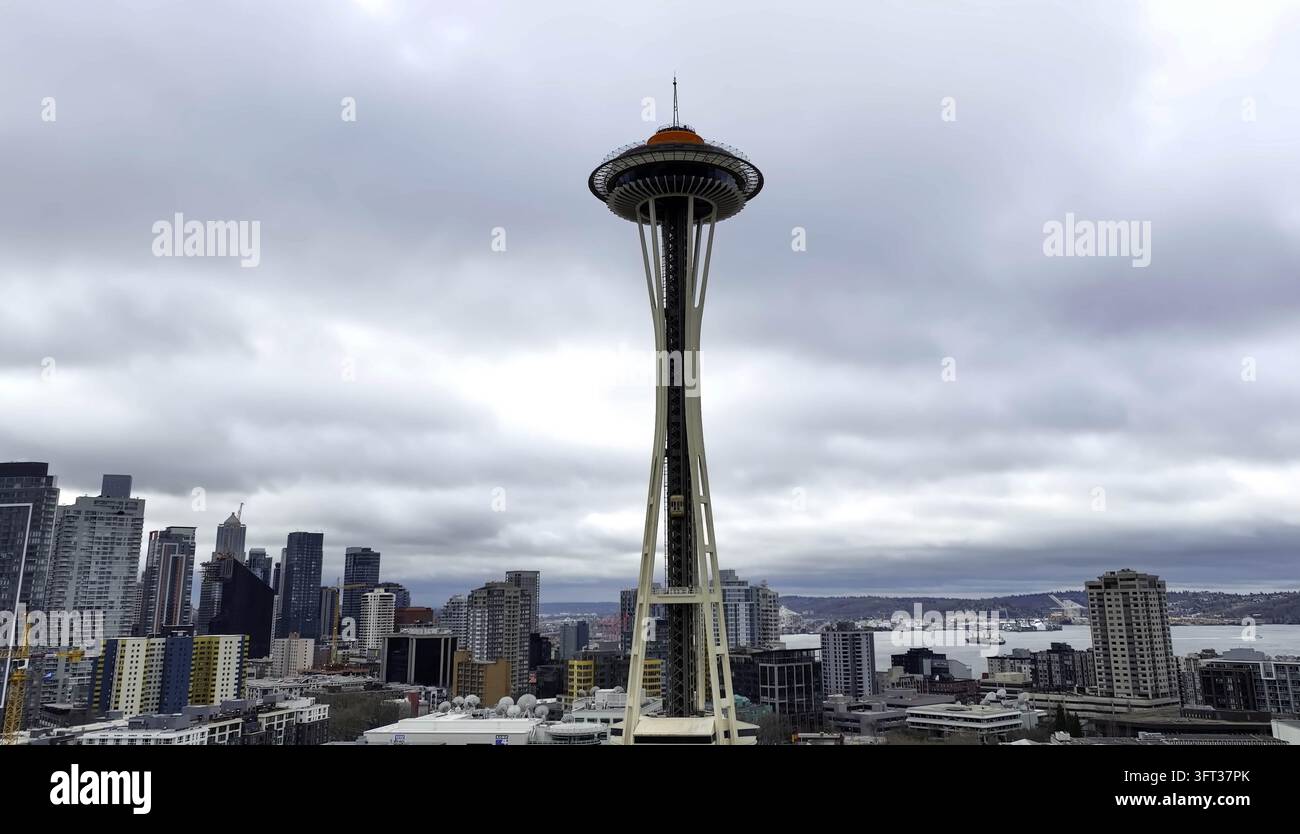Luftaufnahme des Space Needle, der über der städtischen Skyline mit modernen Wolkenkratzern und der fernen Bucht unter einem bewölkten Himmel aufragt, Seattle, WA, Vereinigte Staaten Stockfoto
