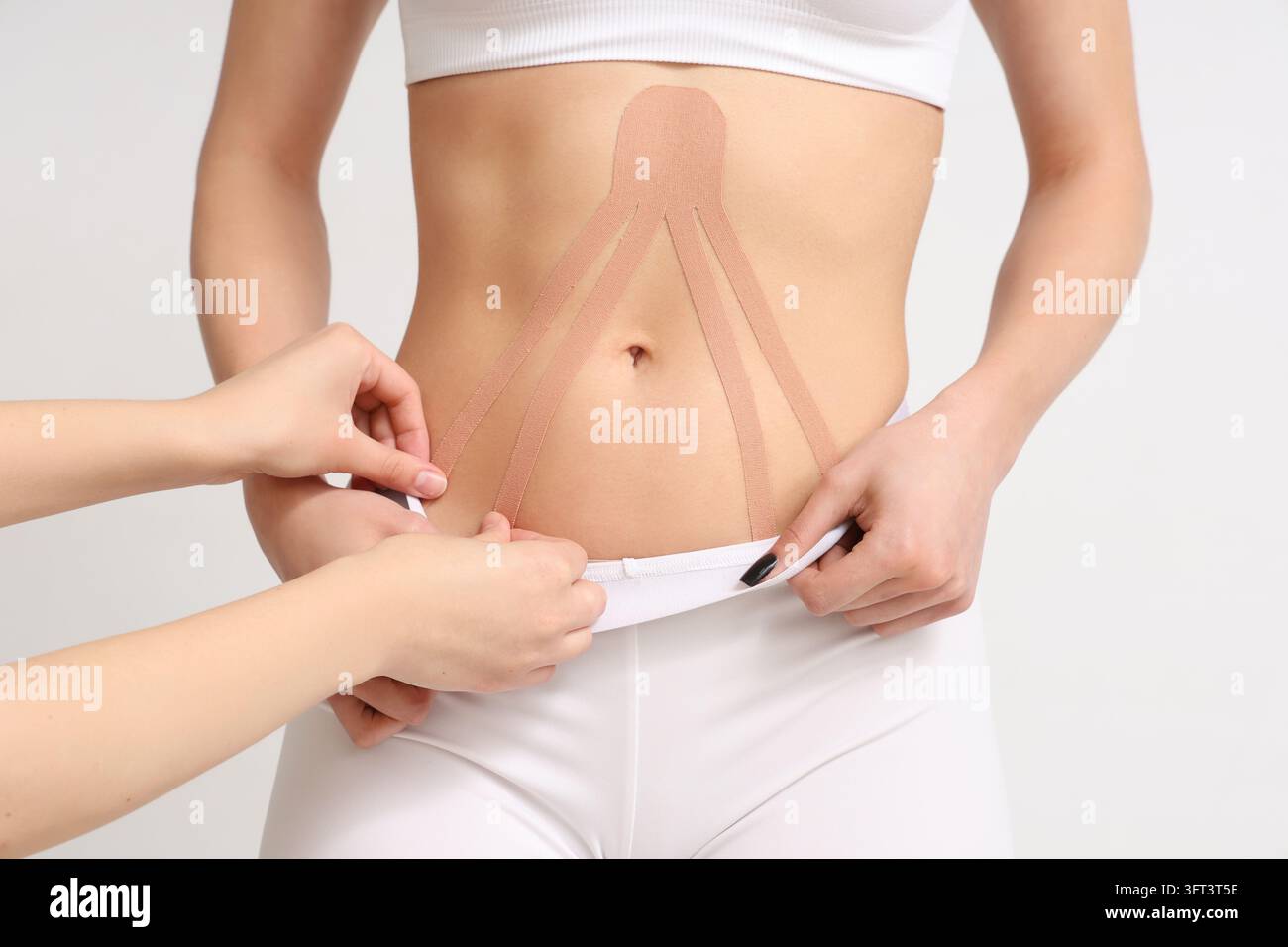 Kinesiologie-Taping zur Bauchunterstützung, Physiotherapie und Verletzungsrehabilitation, Frau erhält therapeutische Taping-Behandlung am Bauch zur Muskelentspannung Stockfoto