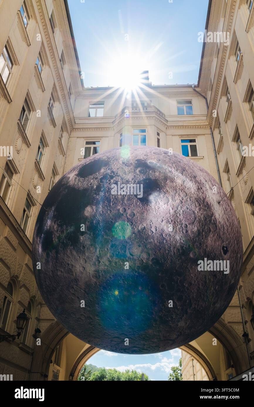 Budapest, Ungarn, 25. Juni 2026: Riesige Mondreplika hängt unter der Piarista koz-Laube, eingerahmt von historischen Gebäuden und heller Sonne. Stockfoto