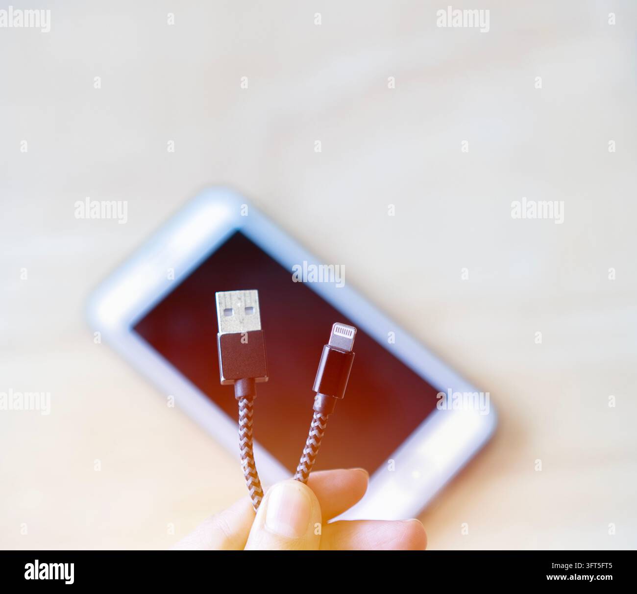 Nahaufnahme von Frauenhänden, die ein USB-Ladekabel an ein Smartphone zu Hause anschließen. USB-Ladekabel-Konzept. Stockfoto