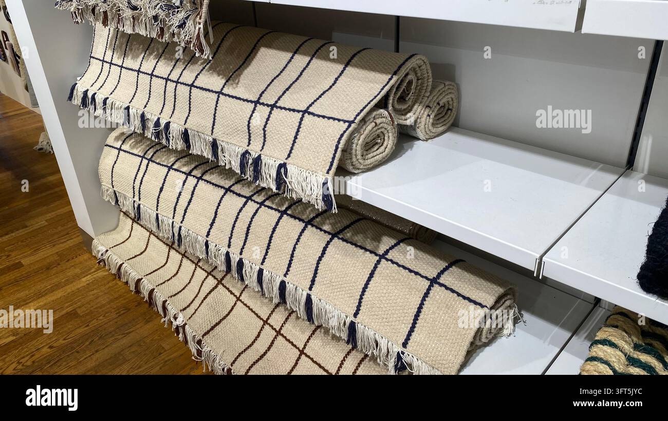 Gerollte beige gewebte Teppiche mit blau-braunen karierten Mustern und fransigen Kanten, die auf Regalen in einem Einrichtungsgeschäft ausgestellt sind Stockfoto