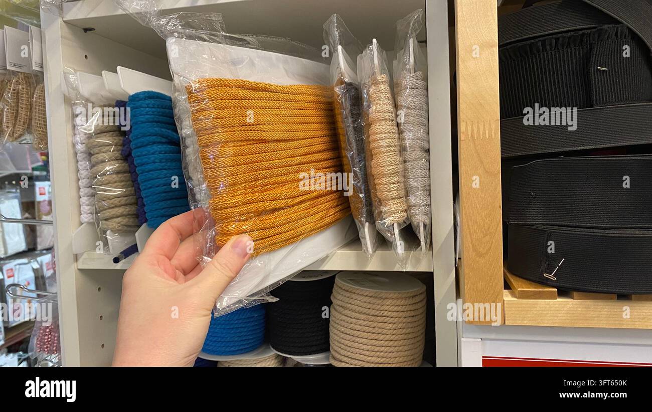 Kunde hält verpackte senfgelbe geflochtene Schnur aus einem Sortiment farbenfroher dekorativer Seile in einem Bastelladen Stockfoto