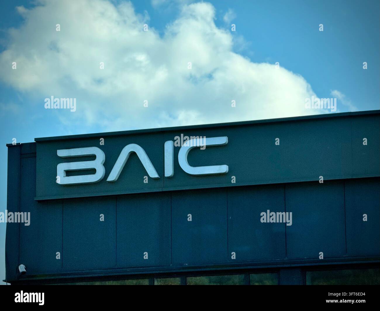 BAIC-Schilder montiert an einer dunkelblaugrünen Gebäudefassade vor einem hellblauen Himmel mit flauschigen weißen Wolken. - Smartphone-aufgenommenes Stockfoto