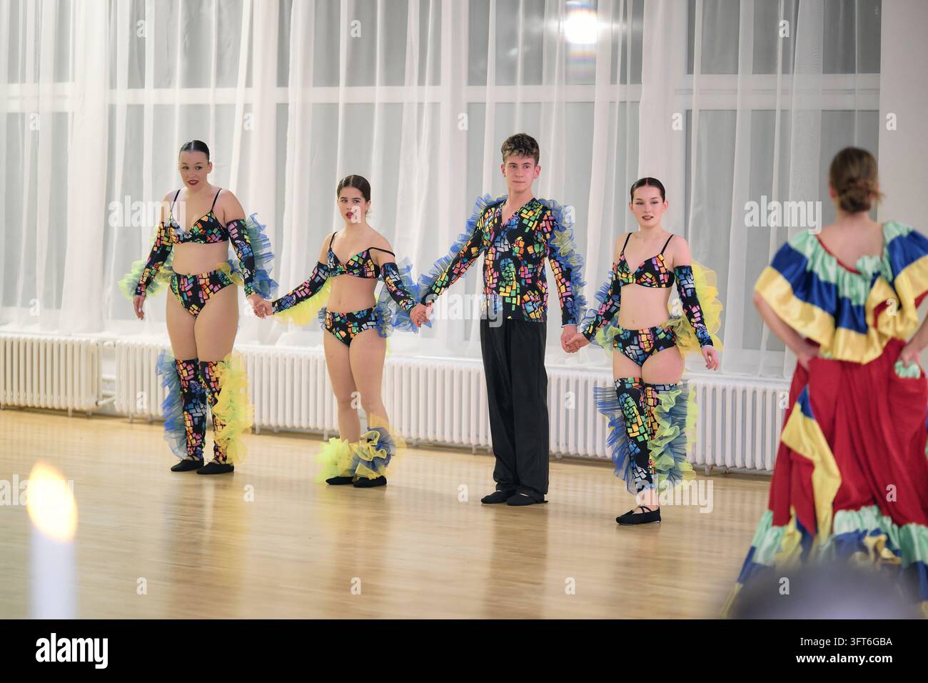 Junge Tänzer in farbenfrohen Blumenkostümen halten sich an den Händen in einer Reihe auf einem Holzboden während einer Aufführung bei einem Ball. Stockfoto