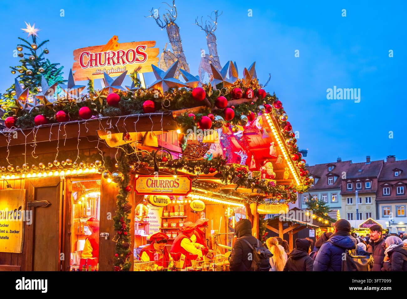 Bamberg, Deutschland – 28. November 2025. Touristen kaufen süße Churros an einem beleuchteten Stand des Bamberg-Weihnachtsmarktes. Stockfoto