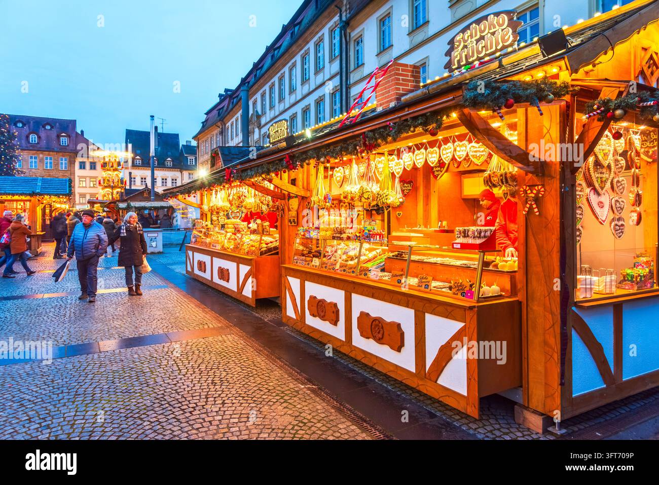 Bamberg, Deutschland – 28. November 2025. Touristen besuchen einen beleuchteten Schokoladenobststand auf dem traditionellen Weihnachtsmarkt. Stockfoto