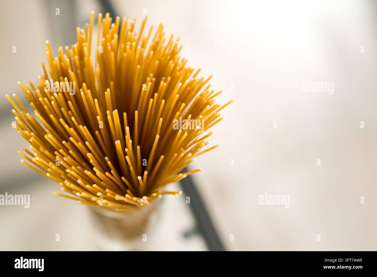 Makroaufnahme von oben eines dichten Bündels trockener, ungekochter gelber Spaghetti, die vertikal in einem Glasbehälter stehen. Stockfoto