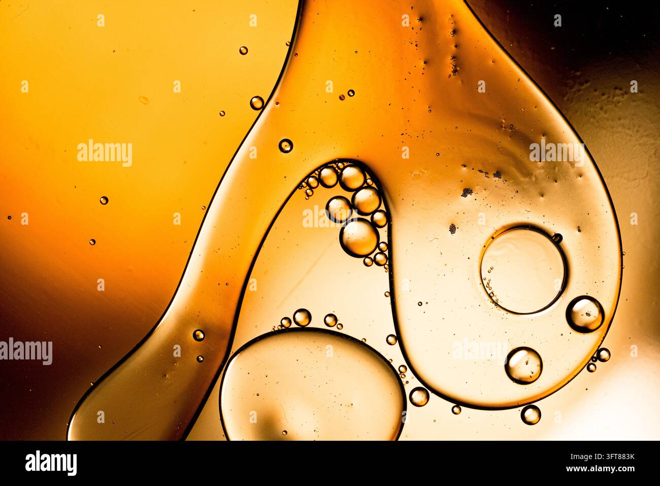 Orange und goldene Flüssigkeit bildet abstrakte Formen und Blasen, die sich auf einer Wasseroberfläche vermischen. Fließeigenschaften und organische Muster Stockfoto