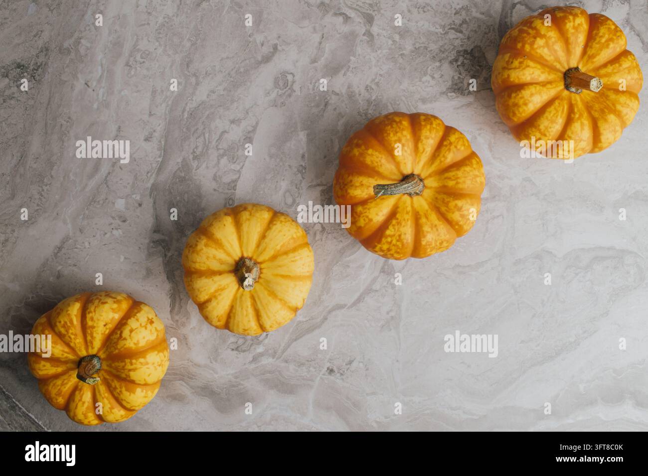 Oberblick auf kleine reife orangefarbene dekorative Kürbisse, die in einer diagonalen Linie auf Marmorhintergrund für ein herbstliches Halloween-Layout angeordnet sind, Stockfoto. Stockfoto