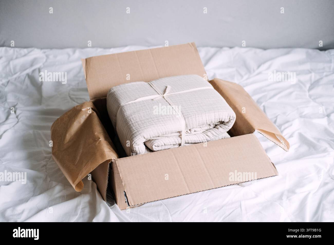 Gefaltetes, gekräuseltes Baumwollgazen-Bettwäsche in einem mit Kraftpapier ausgekleideten Paket, da immer mehr Haushalte Heimtextilien online kaufen Stockfoto