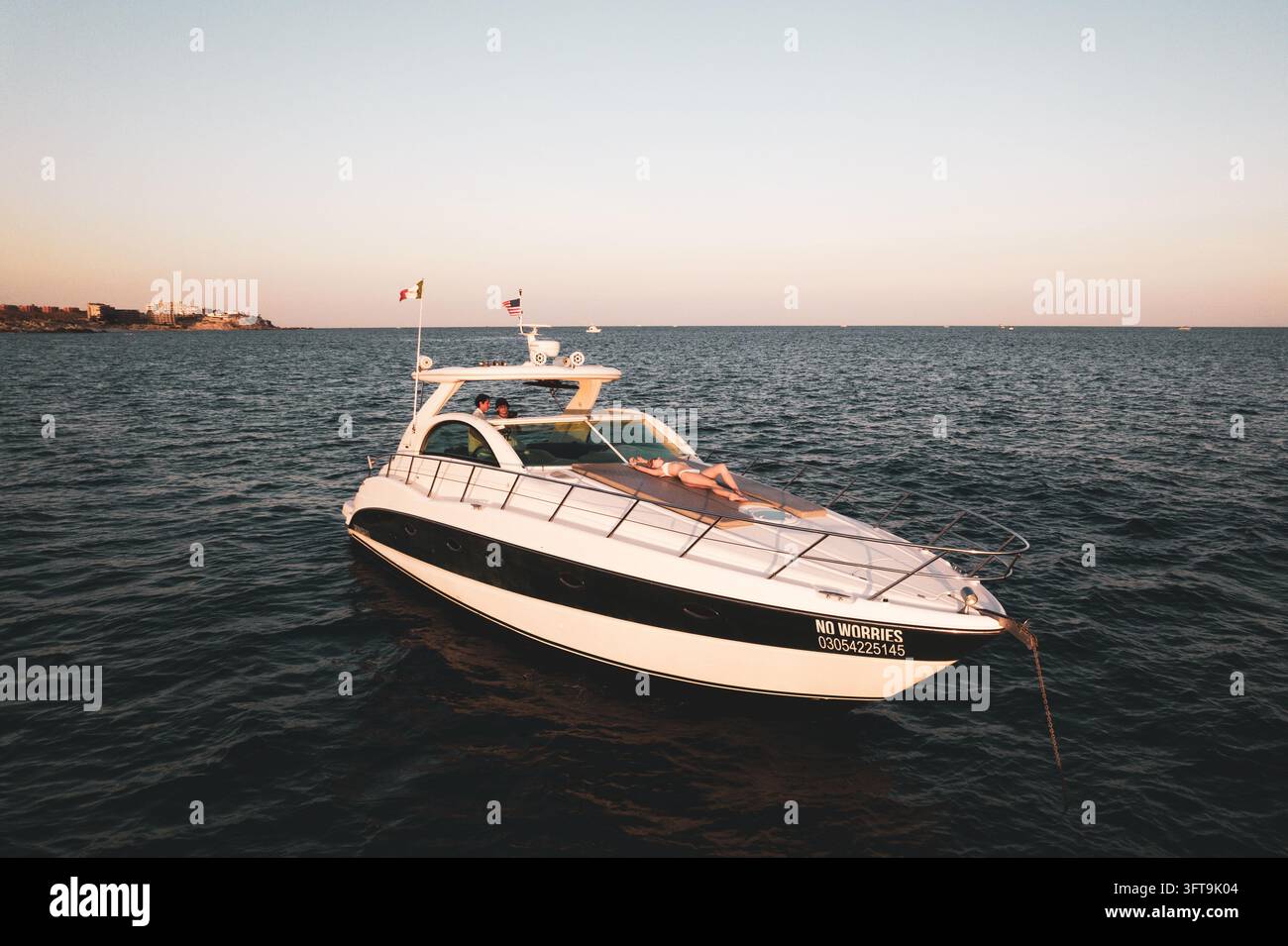 San José del Cabo, Mexiko - 21. Oktober 2025: Luftaufnahme eines weißen Motorboots namens NO WORRIES, das vor El Medano Beach vor Anker liegt, mit einer Frau, die sonnenbadet Stockfoto