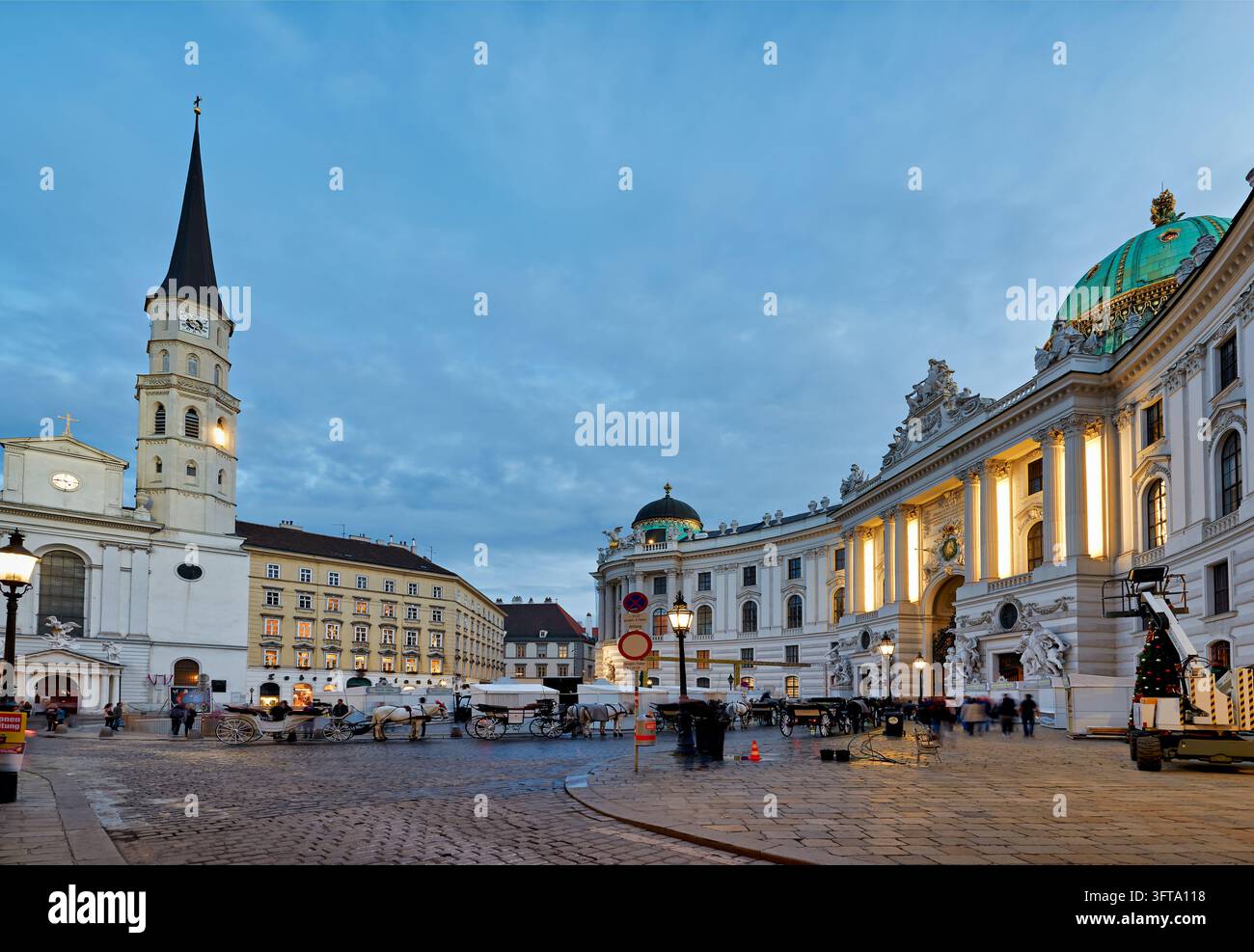 Fiaker Pferdekutschen warten neben der St. Michaels-Kirche und der beleuchteten Michaelertrakt-Kuppel in der Inneren Stadt Wiens, Österreich. Stockfoto