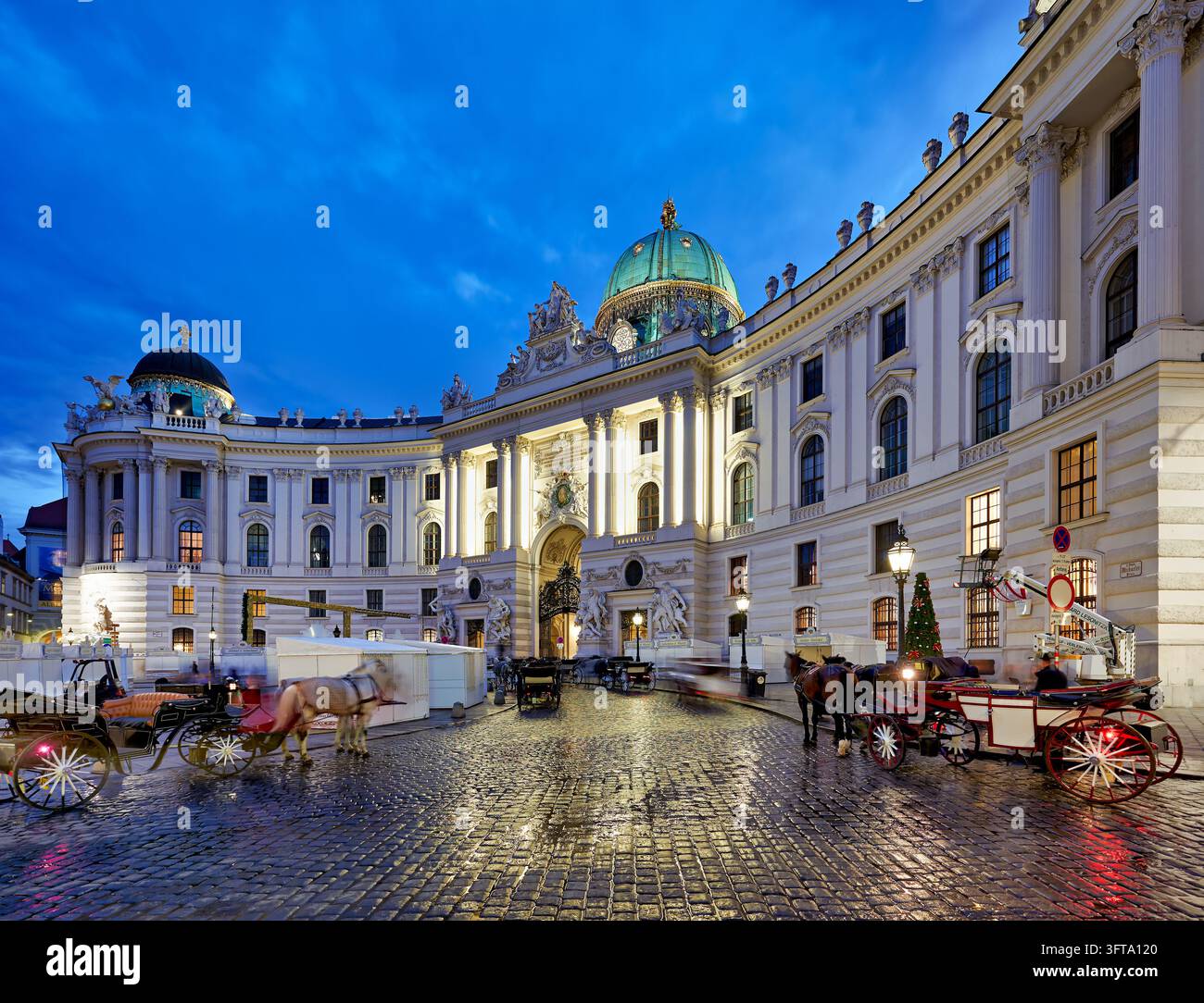 Fiaker Pferdekutschen warten auf nassen Kopfsteinpflaster am Michaelerplatz neben weißen Marktständen in der Hauptstadt Österreichs an einem Novemberabend. Stockfoto