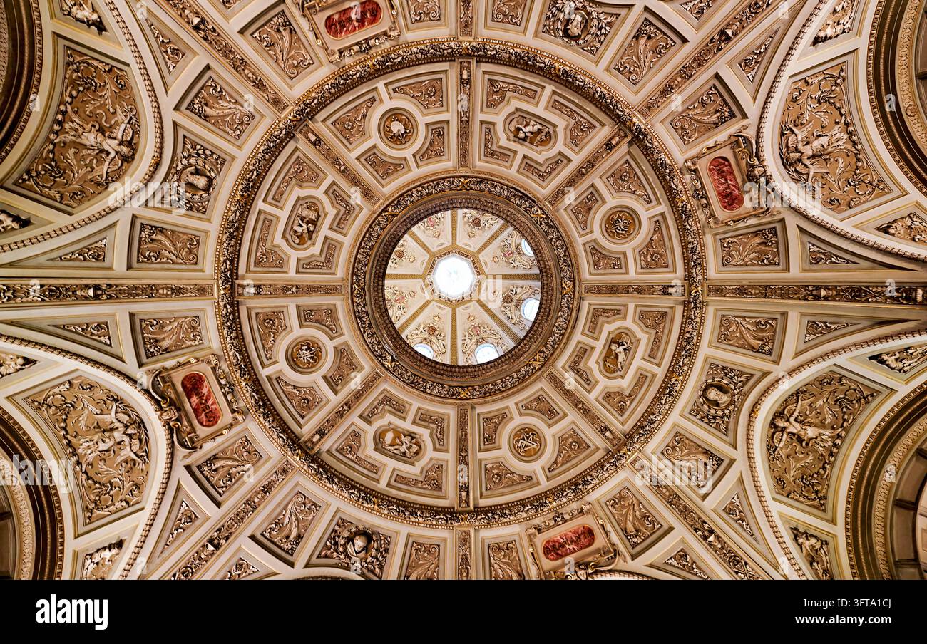 Niedrigwinkelaufnahme von vergoldeten Stuccokassetten, Putten und KünstlerNamenskartuschen um eine von einem Oberlicht beleuchtete Laterne in einer Museumskuppel, Wien, Österreich. Stockfoto
