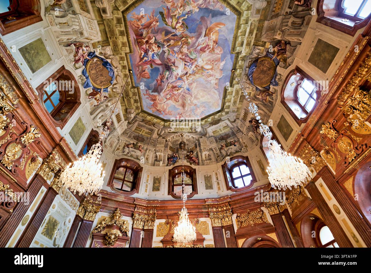 Niedrig angelegte Ansicht einer bemalten allegorischen Decke, vergoldeter Stuck, rote Marmorpilaster und Kristallkronleuchter in einem Innenraum eines Palastes aus dem 18. Jahrhundert. Stockfoto
