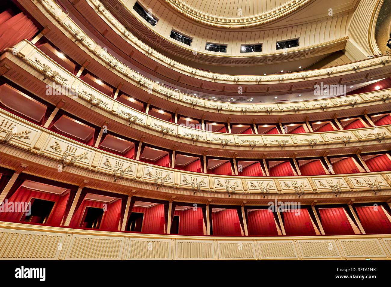 Niedrigwinklige Ansicht des leeren hufeisenförmigen Saals der Wiener Staatsoper in Wien, mit rot gepolsterten Logen und cremefarbenen und goldenen Balkonfronten. Stockfoto