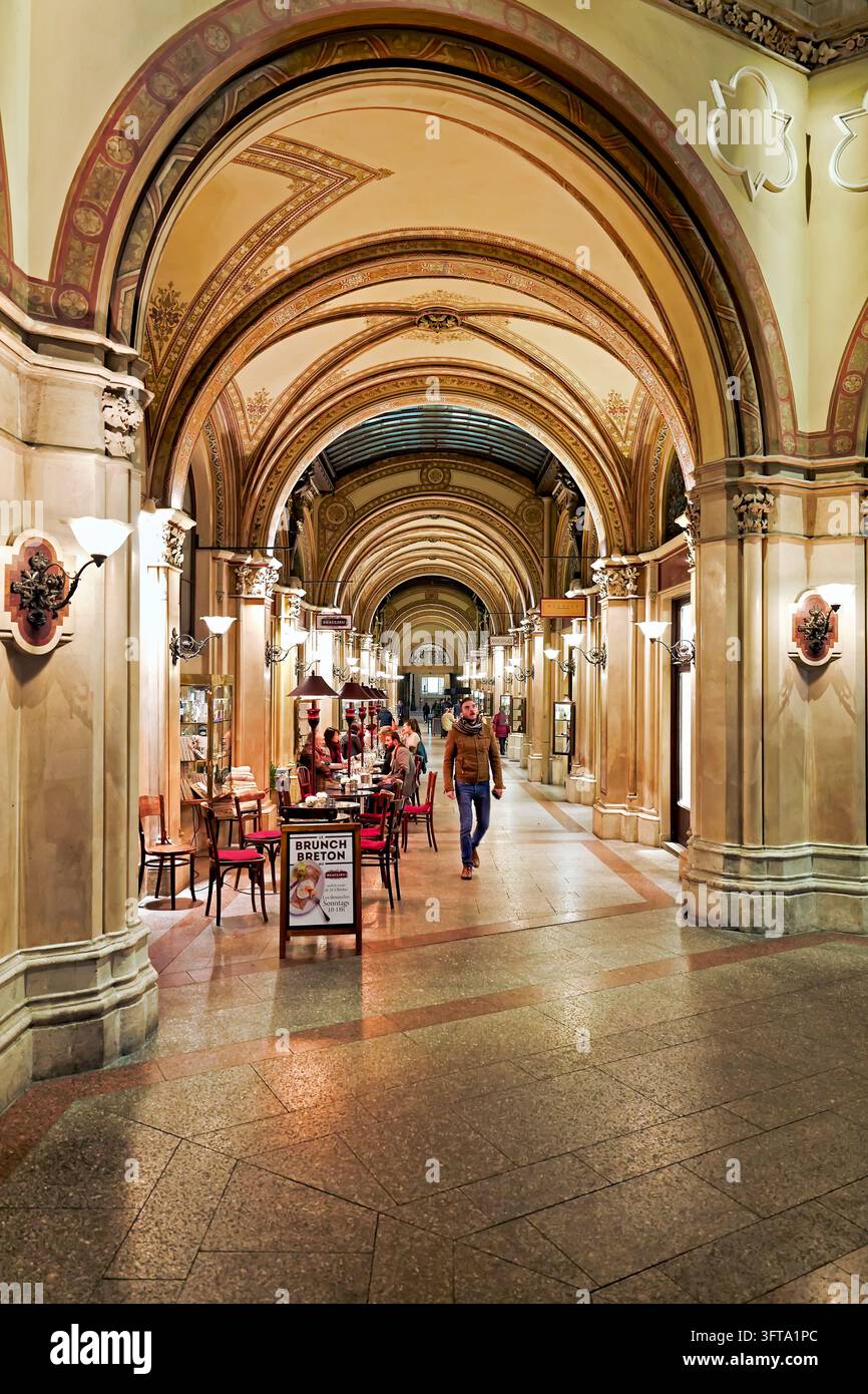 Café-Tische säumen die bemalte gewölbte Einkaufspassage des Palais Ferstel auf der Freyung in der Inneren Stadt Wiens, Österreich, während Fußgänger hindurchgehen. Stockfoto