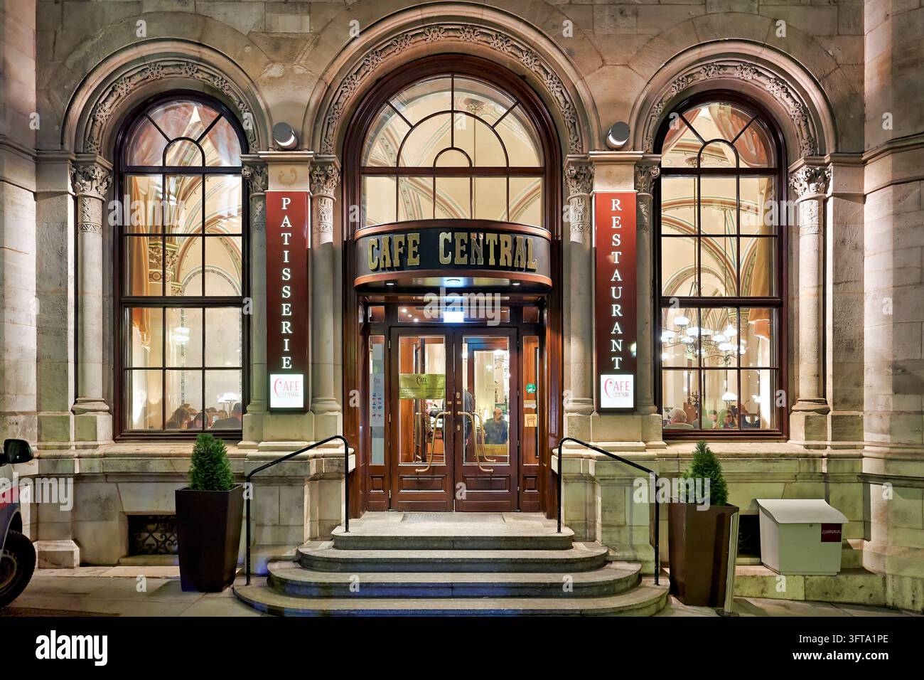 Beleuchteter gewölbter Eingang des historischen Wiener Kaffeehauses im Palais Ferstel, Innere Stadt, flankiert von Konditorei- und Restaurantschildern Stockfoto