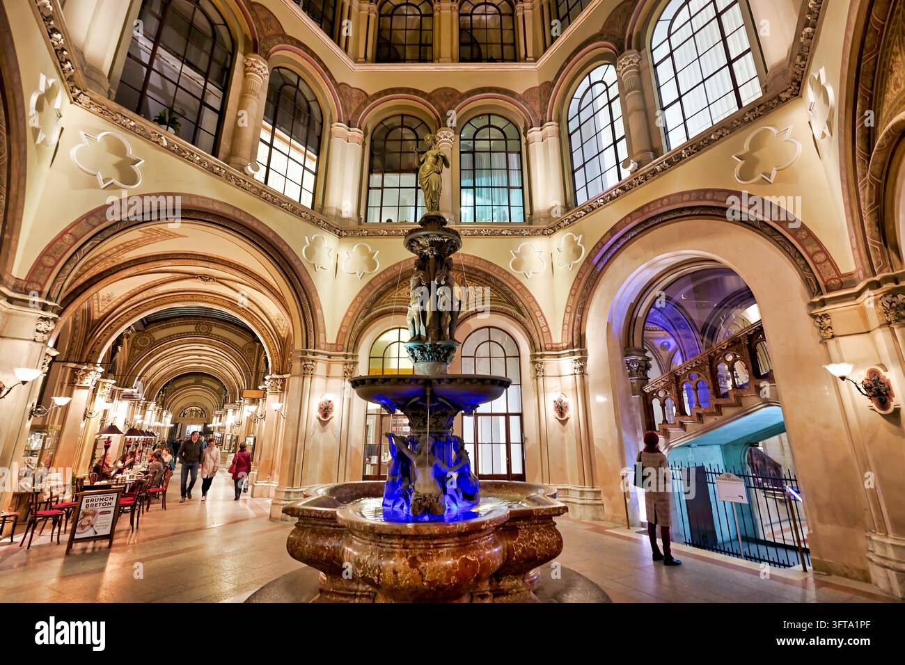 Besucher schlendern an Café-Tischen und einem beleuchteten achteckigen Atrium in der historistischen Einkaufspassage in der Inneren Stadt Wiens, Österreich Stockfoto