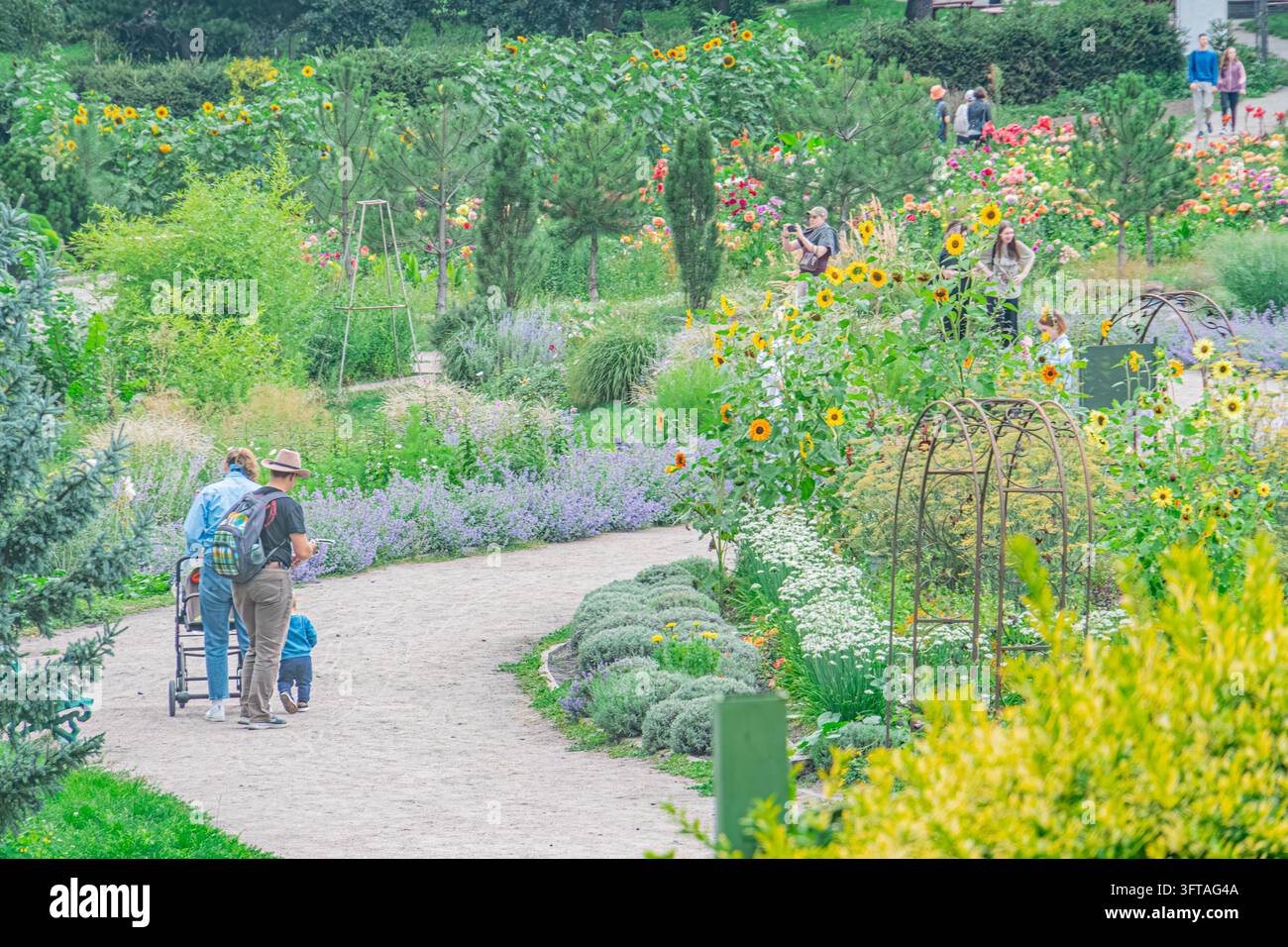 Zwei lässig gekleidete Personen gehen auf einem Kiesweg in einem gepflegten Park in Kiew, Ukraine Der Park bietet lebendige Farben und üppiges Grün Stockfoto