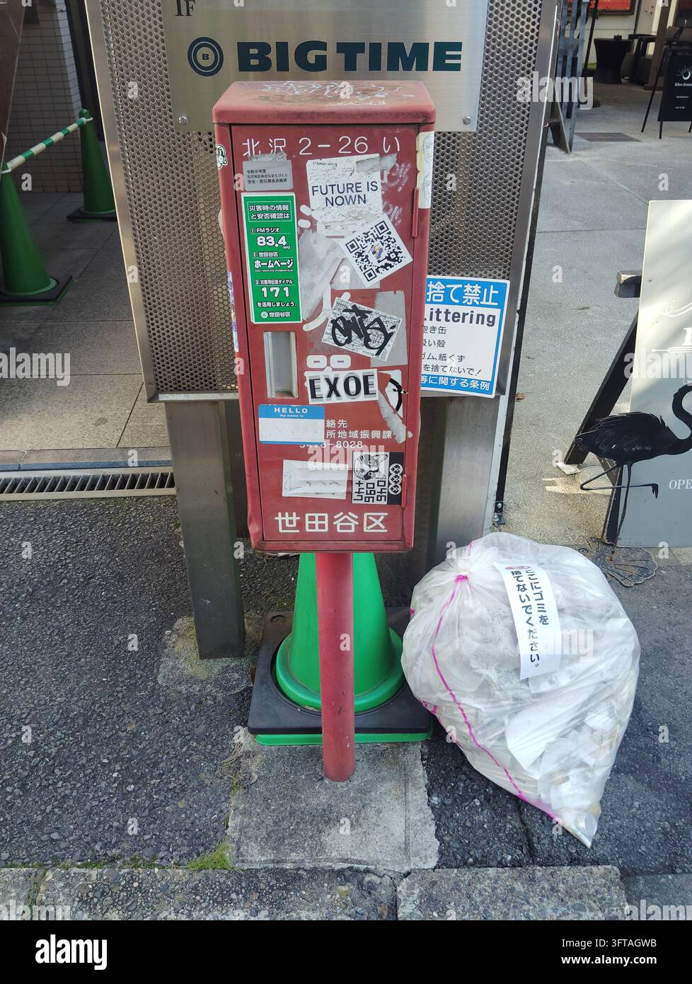 Rote Feuerlöscher-Aufbewahrungsbox mit Aufklebern neben einem Müllsack auf einer Straße in Setagaya, Tokio, Japan. - Smartphone-aufgenommenes Stockfoto