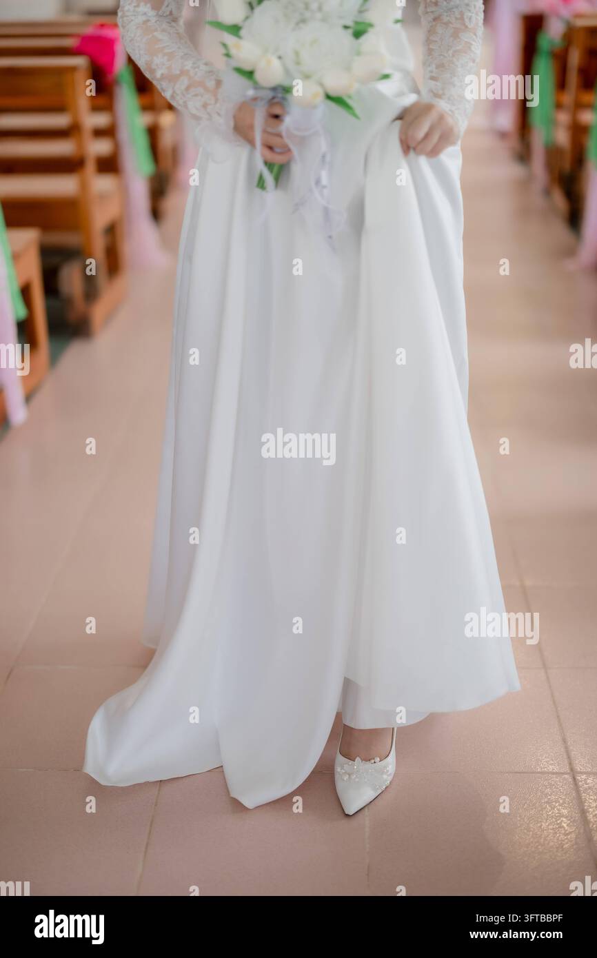 Braut in weißem Kleid mit Blumenstrauß geht durch den Kirchengang Stockfoto