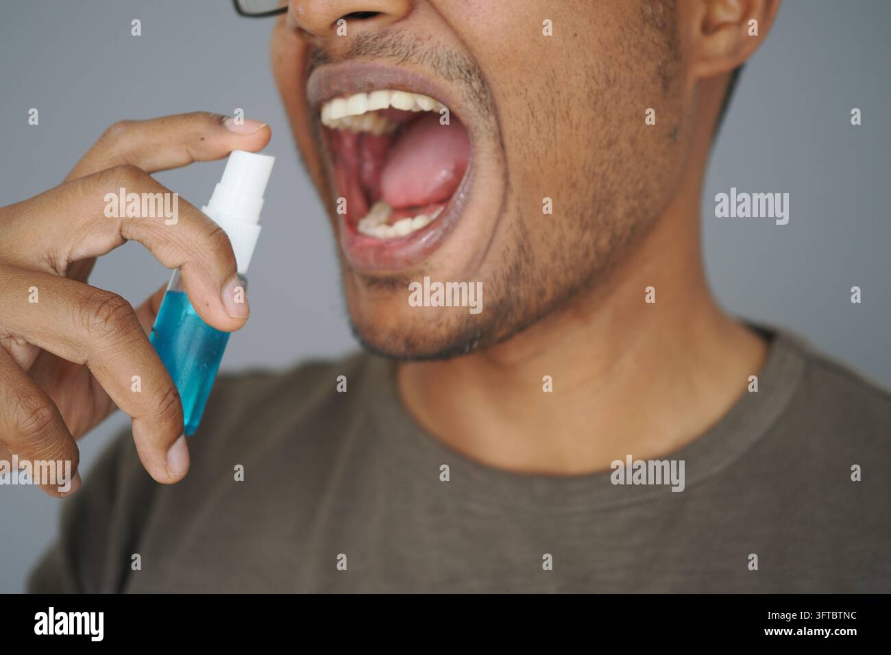 Person, die Mundspray vor grauem Hintergrund verwendet Stockfoto