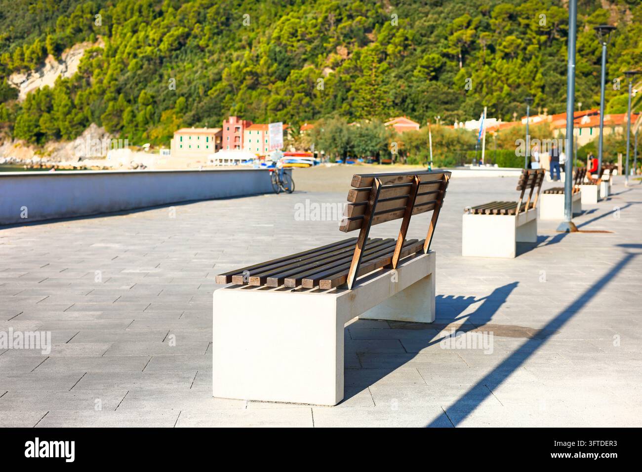 Leere Holzbank sonnige Uferpromenade. Urlaubsentspannung Wellness Ruhe-Stimmung. Reiseziel urbanes Leben Gastgewerbe-Ratgeber. Stockfoto