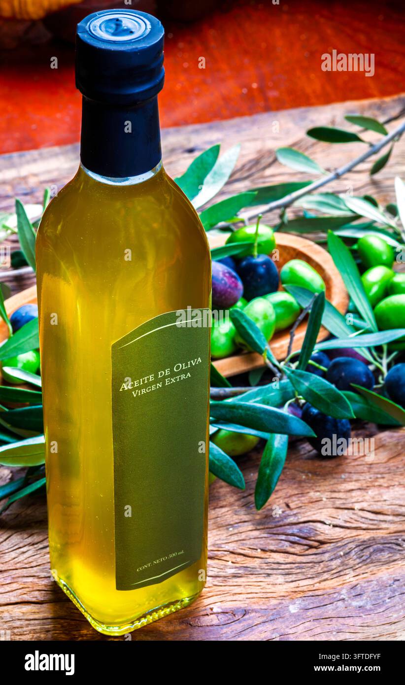 Premium extra natives Olivenöl in einer Glasflasche, umgeben von frischen grünen und schwarzen Oliven auf einem rustikalen Holztisch Stockfoto
