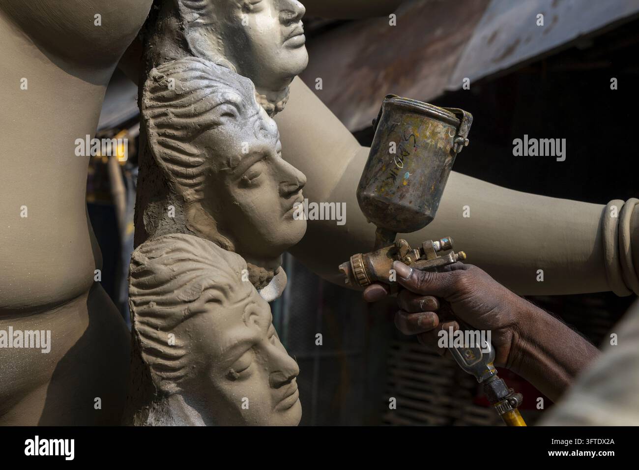 Arbeiter sprüht eine feine Schicht Tonaufschlick auf drei geschnitzte Gesichter einer Statue mit einer Metallpistole in Kumartuli, West Bengal, Kalkutta, Indien Stockfoto