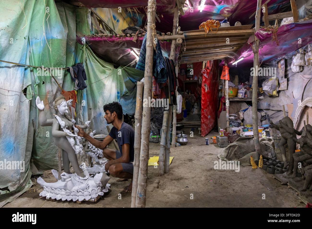 Künstler sitzt neben einer kleinen gebleichten Götzenstatue auf einem Lotos-Sockel in einem langen Schuppen im Bezirk Kumartuli, Westbengalen, Kalkutta, Indien Stockfoto