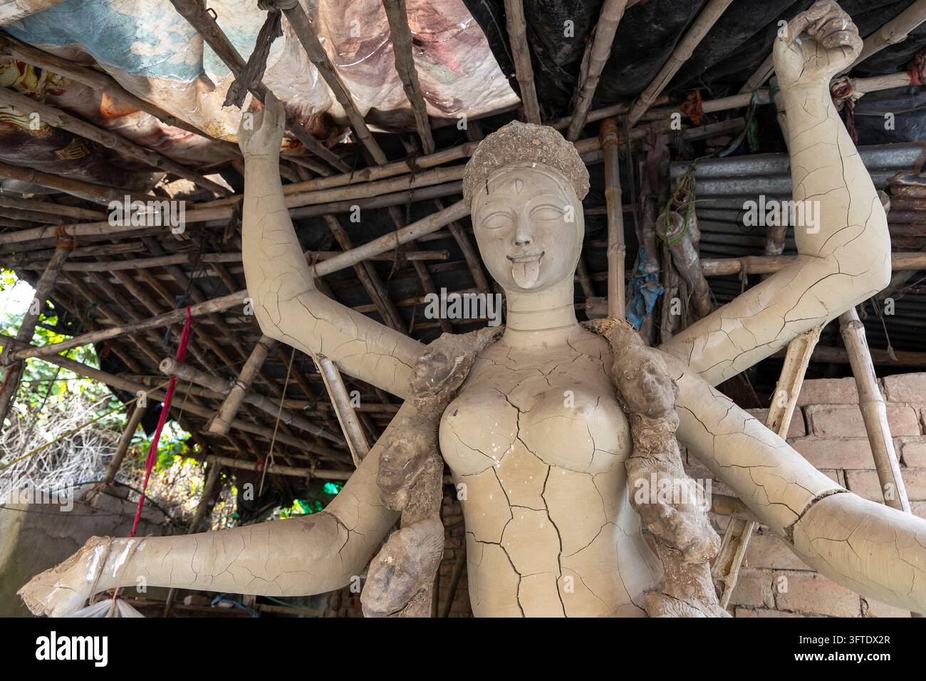 Ungemalte Ton-Göttin mit acht Armen zeigt trocknende Risse unter einem bambusgerahmten Schutzhaus im Bezirk Kumartuli, Westbengalen, Kalkutta, Indien Stockfoto