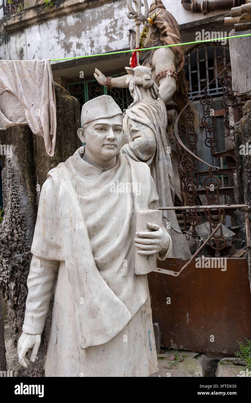 Bemalte weiße Figur eines stehenden Mannes, der ein Buch hält, in einem Eckhof mit Wäsche im Bezirk Kumartuli, West Bengal, Kalkutta, Indien Stockfoto