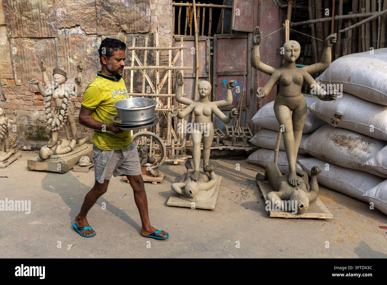 Arbeiter in Shorts und Sandalen hält ein Stahlbecken neben Kali-Figuren aus Ton auf Holzsockeln im Bezirk Kumartuli, Westbengalen, Kalkutta, Indien Stockfoto