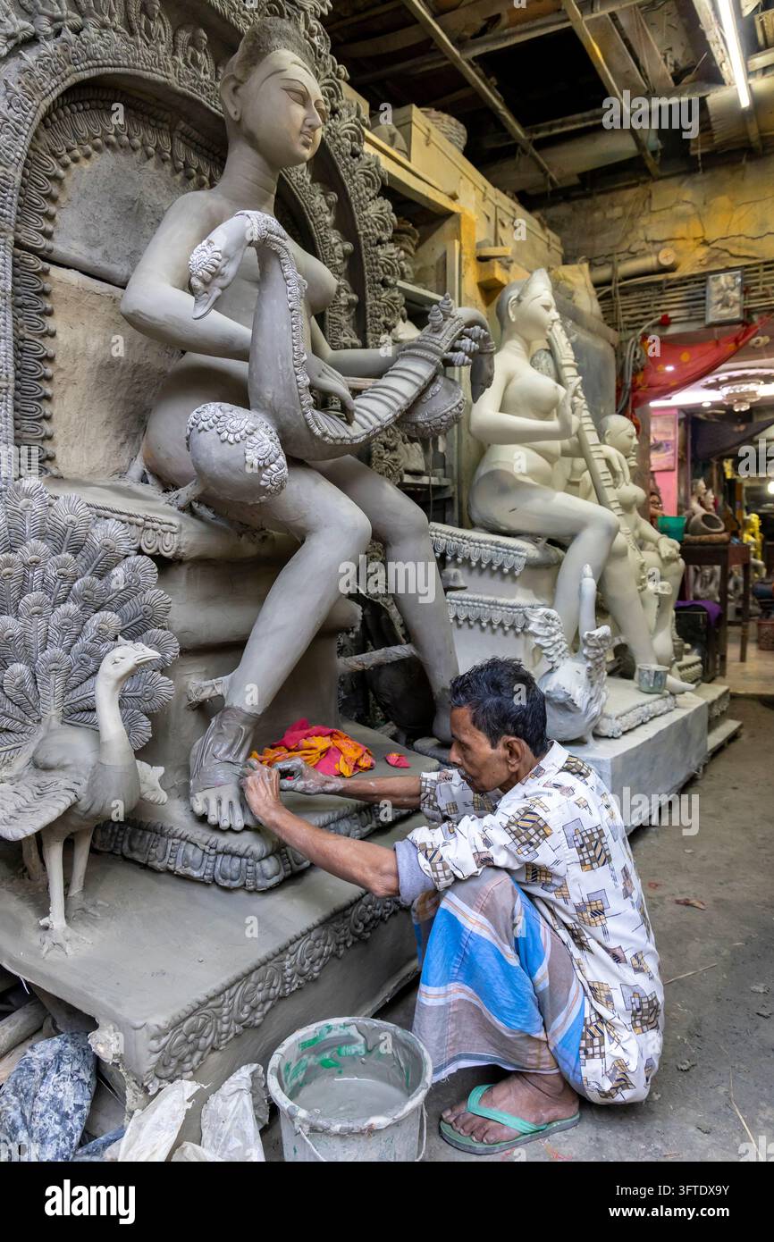 Handwerker in einem gemusterten Hemd und Lungi arbeitet am Sockel eines großen Idols im Bezirk Kumartuli, Westbengalen, Kalkutta, Indien Stockfoto