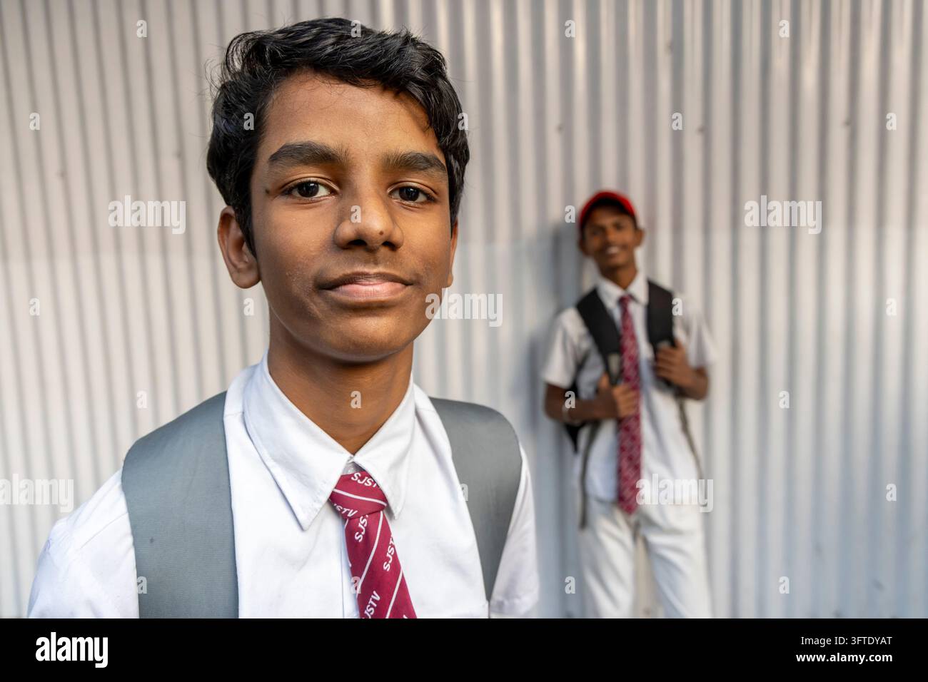 Ein Junge in einem weißen Hemd und einer kastanienbraunen Krawatte mit einem Rucksack schaut in die Kamera, während ein anderer uniformierter Junge lächelt, West Bengal, Kalkutta, Indien Stockfoto