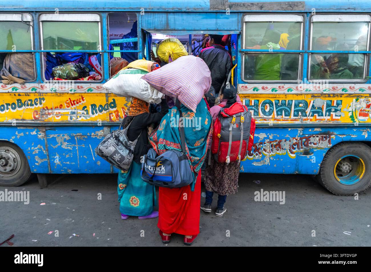Menschen tragen große Säcke und Rucksäcke, während sie in einen abgenutzten blauen Bus klettern, der mit gemalten Blumen verziert ist, West Bengal, Kolkata, Indien Stockfoto