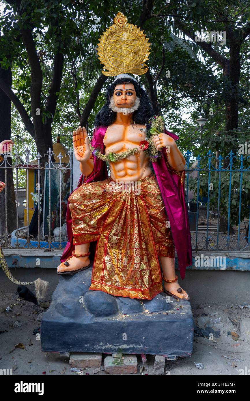Gemalte Figur mit einer goldenen Krone, einer erhobenen Hand und einem Blumengirlande trägt einen orangefarbenen Rock unter grünen Bäumen, West Bengal, Kalkutta, Indien Stockfoto