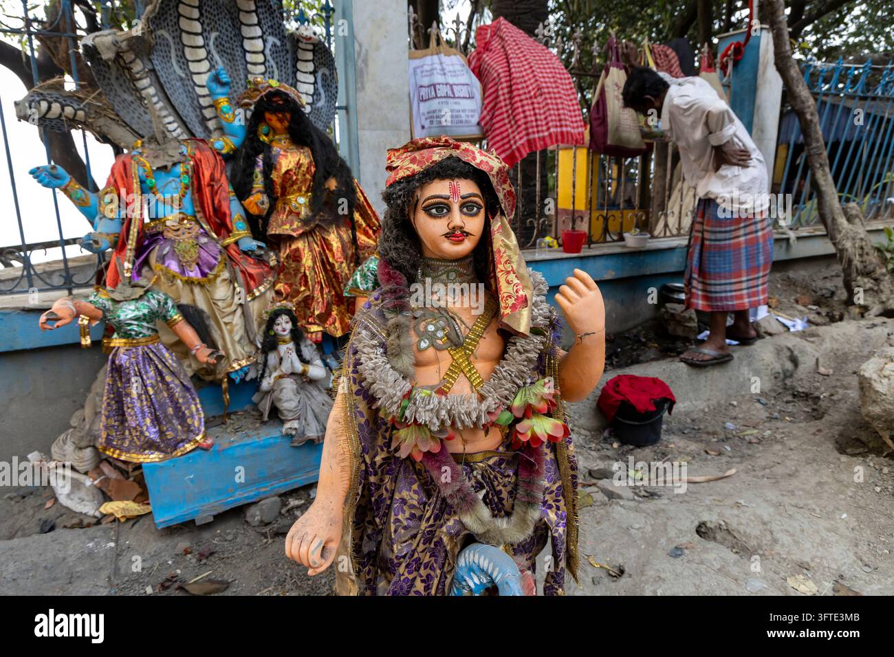 Gruppe von Festival-Idolen mit Kobra-Kappen und farbenfrohen Kostümen steht nahe einem Eisenzaun, während sich ein Mann dahinter bückt, West Bengal, Kalkutta, Indien Stockfoto