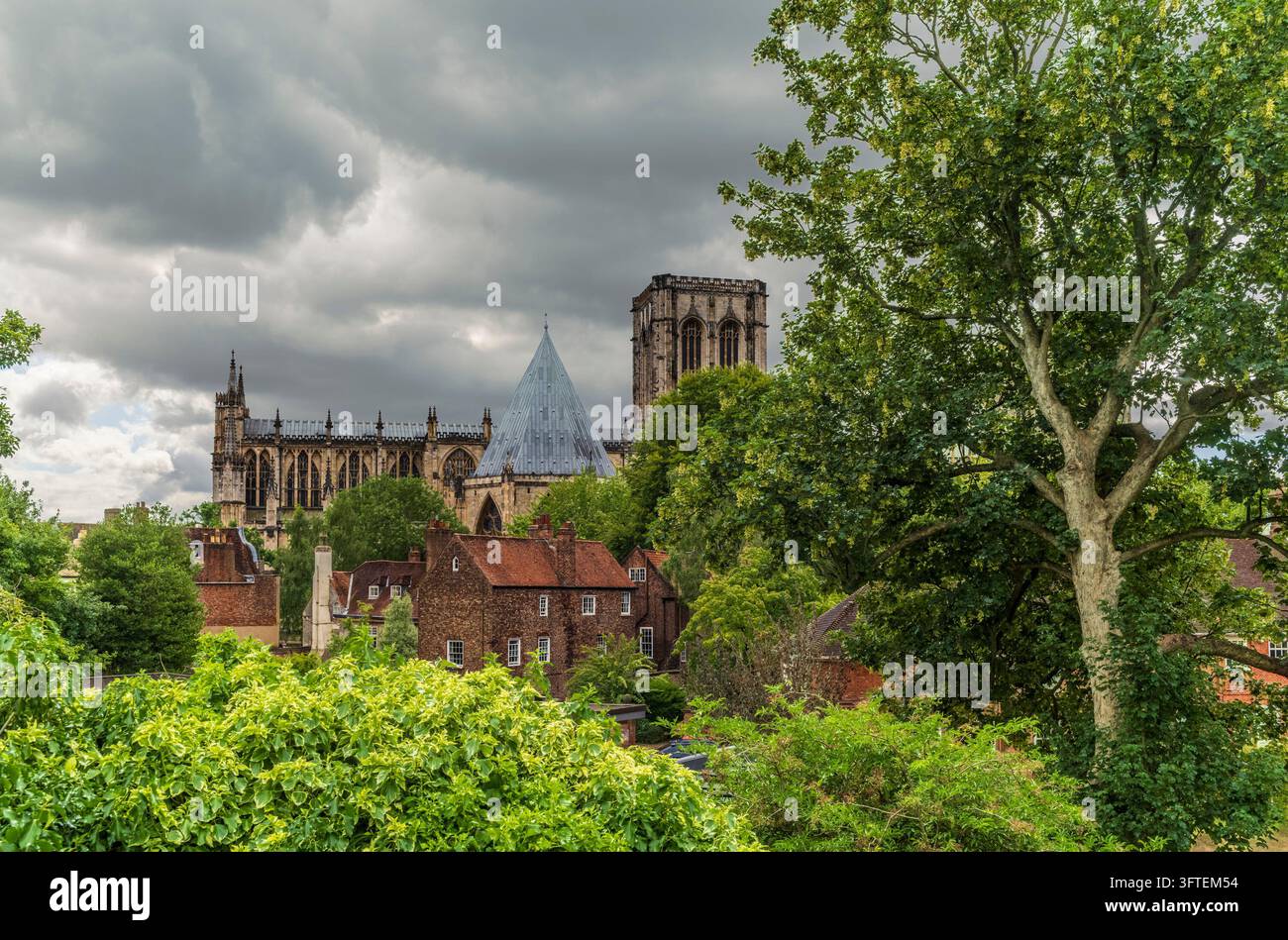 York Minster Gotische Kathedrale über grünen Bäumen und Ziegeldächern unter einem stürmischen Himmel Stockfoto