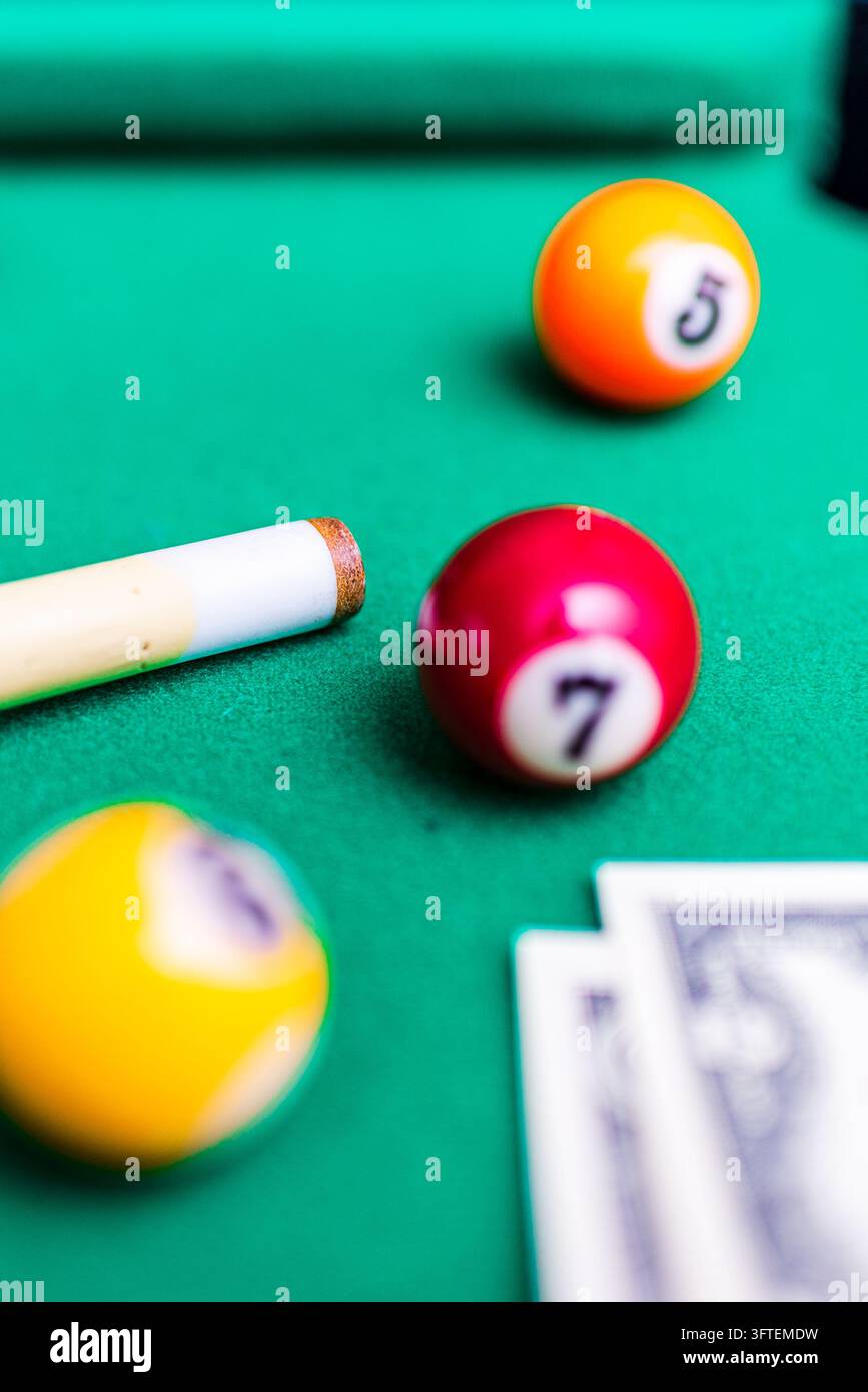 Roter Billardball mit der Nummer 7 mit Queue-Spitze und Geld auf grünem Tisch mit vertikalem Kopierraum. Stockfoto